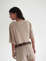 Top corto color beige de tejido de punto con mangas cortas y cuello redondo. Presenta un bordado dorado en el pecho.