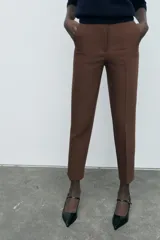 Pantalón marrón de tiro alto con costuras marcadas en delantero y espalda, bolsillos delanteros de vivo y cierre frontal con cremallera, botón interior y gancho metálico.