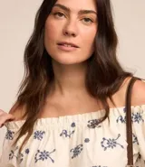 Blusa de hombros descubiertos color crema con estampado floral azul, mangas cortas abullonadas y detalle de hilo metalizado.