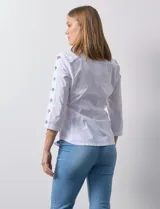 Camisa blanca de algodón con cuello clásico, solapa y escote en V. Tiene mangas tres cuartos con detalle de aberturas cruzadas. Presenta dos bolsillos delanteros aplicados y laterales en tejido modal.