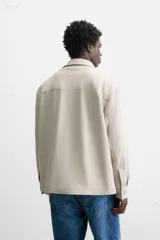 Sobrecamisa color beige de corte relaxed fit, con cuello solapa, manga larga con puños abotonados, bolsillos de plastrón con solapa en el pecho y bolsillos de vivo en la cadera. Cierre frontal con botones.