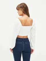 Blusa crop top negra con escote cuadrado, mangas largas abullonadas y lazo ajustable en el centro del busto.