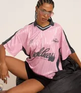 Remera rosa con cuello polo gris y rayas verticales. Estampado frontal con la palabra "gobline" en letras cursivas y la frase "in my best era". Diseño oversized con mangas cortas y recortes laterales en color negro.