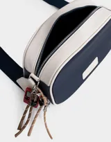Bandolera de cuerina azul marino y beige con correa regulable azul y charm lateral decorativo. Tiene cierre superior y tag frontal con logo "The Brunch Club".