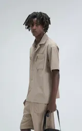 Camisa beige de manga corta, estilo técnica, confeccionada en microfibra liviana. Con doble bolsillo frontal y broches en lugar de botones.