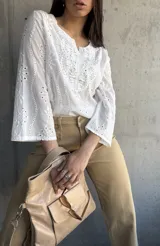 Blusa blanca de algodón con bordado broderie, escote en V y mangas largas.