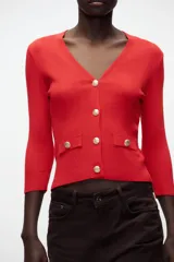 Chaqueta de punto roja con escote en pico, manga francesa y cierre frontal con botones dorados.