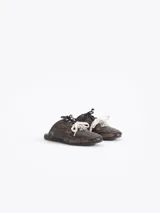 Zapatilla tipo mule (sin talón) de cuero vacuno, color celeste con efecto gastado y detalles de recortes. Presenta un logo estilizado en el lateral y cordones anchos de color beige y marrón.