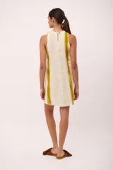 Vestido corto sin mangas, con cuello redondo y estampado a rayas verticales en tonos blanco y amarillo. Confeccionado en lino italiano y detalle desflecado en cuello y ruedo.