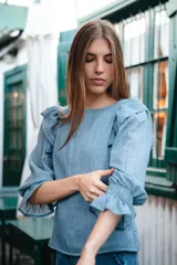 Blusa celeste de algodón con mangas largas abullonadas y puños elastizados con volados. Presenta volados en los hombros y escote redondo.