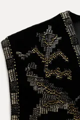 Chaleco abierto de terciopelo negro con bordados dorados y forro interior a tono.