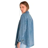 Camisa de jean celeste, de corte amplio, con cuello clásico, cierre frontal con botones, mangas largas con puños abotonados, dos bolsillos con solapa abotonada en el pecho y aberturas laterales en el ruedo.
