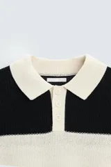 Sweater tipo polo de punto con rayas horizontales anchas en color negro y crudo, con cuello clásico y cierre de dos botones.
