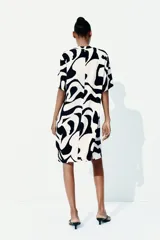 Vestido túnica a la rodilla de viscosa con estampado abstracto en blanco y negro. Tiene cuello mao, abertura en V, corte holgado, hombros caídos, mangas cortas, bajo recto y tajos laterales.