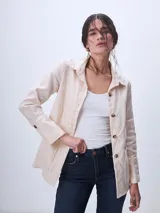Sobrecamisa color crema con cuello camisero, cierre frontal con botones marrones, mangas largas con puños abotonados y bolsillos laterales.