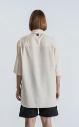 Camisa oversize color crema con cuello clásico, cierre frontal con botones marrones y mangas cortas.