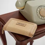 Billetera mediana color beige con textura croco, cierre alrededor y logo Lincoln's.