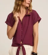 Blusa color borgoña de viscosa texturizada, con cuello, abotonada al frente, mangas cortas con dobladillo y lazo en la cintura.