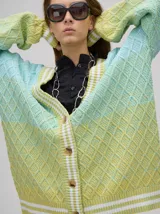 Cardigan tejido de punto con patrón de rombos en degradé de grises y blanco. Tiene corte oversize, mangas largas y cierre frontal con botones.