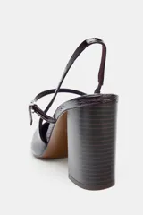 Zapato tipo mercedita destalonado de charol color borgoña oscuro, con punta cuadrada. Posee una tira delantera con hebilla metálica y una tira trasera elástica. El tacón es alto y de bloque.