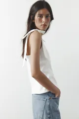 Top blanco de tejido elástico con escote cuadrado y tirantes anchos con lazos decorativos.