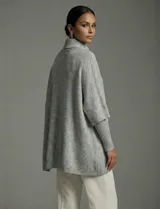 Capa o poncho tejido color verde esmeralda, con cuello polera alto que se cierra con un botón grande en el lateral. Presenta mangas cortas estilo japonesa y un calce amplio.