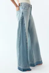 Pantalón de jean de tiro medio con cinco bolsillos, corte wide leg y detalle de tejido con lavado lateral combinado. Cierre frontal con cremallera y botón.