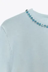 Jersey celeste de punto con cuello redondo adornado con abalorios joya y manga larga. Tiene cierre en la espalda con abertura y botones.