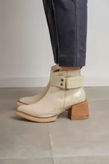 Bota corta de cuero marrón con puntera redondeada y taco cuadrado. Presenta una correa con hebilla alrededor del tobillo y cierre lateral.