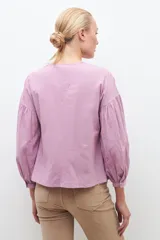 Blusa lila con bordados, de mangas largas abullonadas y cuello en V.