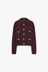 Chaqueta de punto color borgoña, con cuello camisero y manga larga. Tiene falsos bolsillos con solapa en el delantero y cierre frontal con botones metálicos dorados.