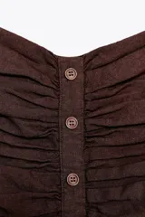 Top bustier marrón de lino con escote recto, hombros descubiertos, detalle de frunces, falsos botones delanteros y nido de abeja elástico en la espalda.