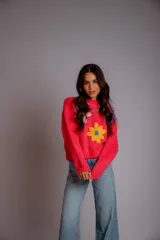 Buzo de punto color lila, con cuello redondo, mangas largas y diseño holgado. Presenta tres flores bordadas en el frente: una rosa claro, una azul y una amarilla con centro azul.