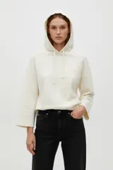 Buzo con capucha color crudo o natural, de manga larga y calce holgado. Presenta un diseño sutil bordado en el frente.