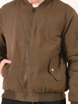 Chaqueta tipo bomber color verde militar, con cierre frontal, cuello y puños acanalados. Presenta bolsillo utilitario con cierre en la manga izquierda y bolsillos frontales con solapa y broche.