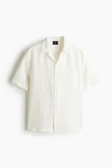 Camisa de manga corta color blanco, de corte recto, con cuello resort, cierre frontal con botones y bolsillo de parche en el pecho.