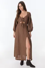 Vestido color beige de lino, con escote en V, mangas largas abullonadas y lazos frontales. Tiene corte a la cintura y falda larga con tajo frontal.