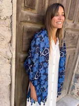 Chalina rectangular de tela ligera color azul con estampado de flores blancas y borlas en los extremos.