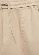 Pantalón color beige de tiro medio, corte recto y diseño largo. Cuenta con dos bolsillos delanteros, cierre de lazo y dos bolsillos de parche en la parte posterior.