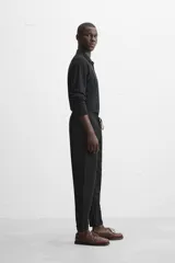 Pantalón negro de corte cropped, con cintura elástica ajustable con cordón, bolsillos laterales y traseros de vivo. El bajo tiene terminación con vuelta.
