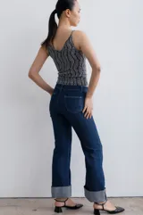 Pantalón de jean azul oscuro con corte acampanado, tiro medio y dobladillo en el ruedo. Presenta costuras marcadas en el frente y estampado abstracto en tonos grises y blancos en el interior del dobladillo.