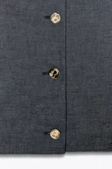 Chaleco azul con textura, corte entallado con pinzas y cierre frontal con botones dorados.