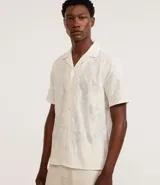 Camisa de manga corta color crema con bordado floral texturizado, cuello solapa y abotonadura frontal.