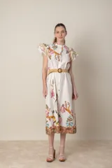 Vestido midi camisero de algodón color natural con estampado de flores, animales y ramas en tonos rojo, marrón, verde y azul. Tiene cuello mao, mangas cortas con volados, bolsillos laterales y cinturón de soga color beige.