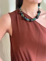 Collar corto con cuentas grandes de madera color marrón oscuro, separadores de metal con incrustaciones de turquesas y cuentas pequeñas turquesas. Cierre con cadena de acero quirúrgico y ganchito para regular el largo.