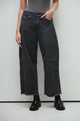 Pantalón de jean negro de pierna ancha, tiro medio y pinzas marcadas, con lavado stonewash y botamanga deshilachada.