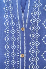 Camisa azul con bordados blancos, de cuello redondo con escote pico y manga larga.