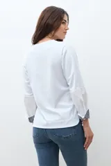 Remera blanca de manga larga con puños doblados que muestran un estampado vichy (cuadros) en azul marino y blanco. Tiene cuello redondo y un calce relajado.