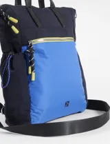 Mochila tipo shopper de poliéster color negro, con asas de cuero sintético negro y cordones ajustables laterales con terminaciones en rojo y blanco. Presenta un bolsillo frontal con cierre metálico plateado y un pequeño logo bordado en la parte inferior.