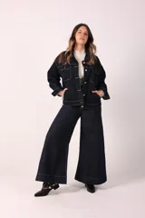 Chaqueta de denim azul oscuro, de corte holgado, con cuello clásico, cierre frontal con botones metálicos, cuatro bolsillos frontales y costuras en hilo color crudo.